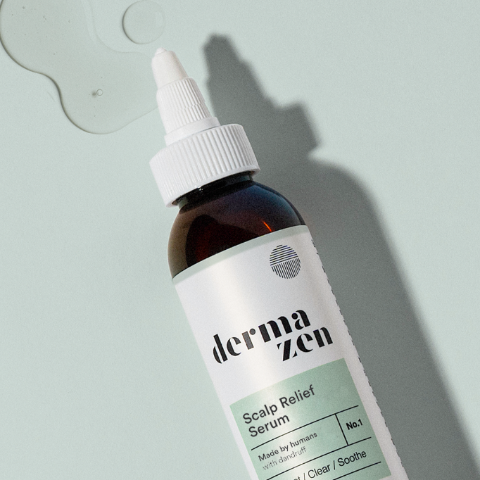 Bottle of Dermazen Scalp Relief Serum on a light background with drops of the serum beside it.